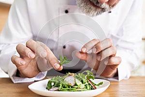 Male cook chef decorating garnishing prepared salad dish on the plate in restaurant commercial kitchen.