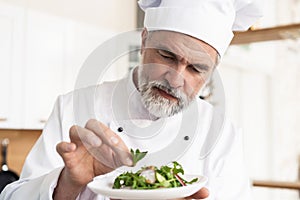 Male cook chef decorating garnishing prepared salad dish on the plate in restaurant commercial kitchen.