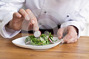 Male cook chef decorating garnishing prepared salad dish on the plate in restaurant commercial kitchen.