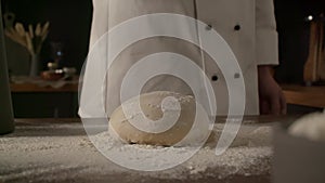 Male cook kneading dough with flour on the kitchen table, cook in slow motion