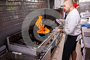 Male cook making flambe seafood at stove in restaurant kitchen