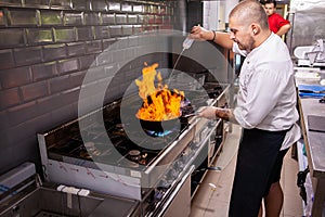 Male cook making flambe seafood at stove in restaurant kitchen