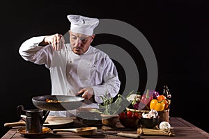 Male cook in white uniform and hat putting herbs on food plate with vegetable photo