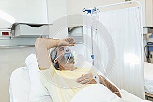 Male coronavirus patient looking away while resting on hospital bed. Man is wearing oxygen mask. He is in hospital during pandemic