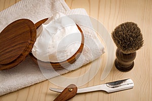 Male cosmetic products and supplies used by men to shave concept with a straight razor, towel, shaving brush and foam on wood