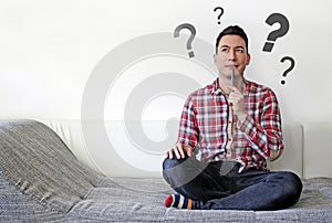 Male on the couch contemplating options with questions marks in the background