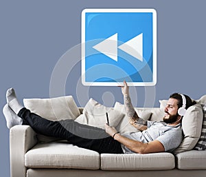 Male on a couch holding a rewind button icon photo
