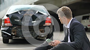 Male counting euros, looking at damage car after traffic accident, repairs cost