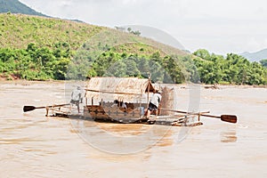 Male couple rafting the bamboo raft house on the Kok River, tropical mountain view riverside. Northern Thailand