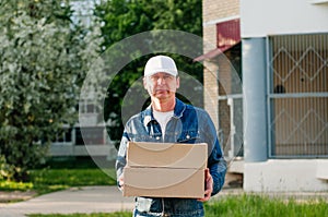Male courier in the blue costume and a cap taking out mail carton boxes from the white van on the sunny day in the street. Outdoor photo