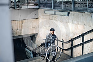 Male courier delivering packages in city, carrying bicycle up the stairs.