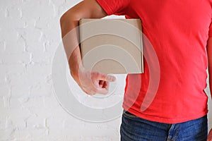 A male courier in a red uniform holds a cardboard box in his hands against a background of a white brick wall. Delivery service