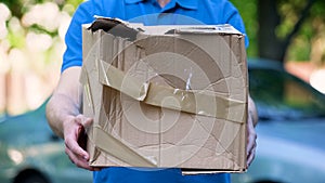 Male courier showing damaged box, cheap parcel delivery, poor shipment quality