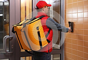 Male courier with thermo bag pushing intercom button. Food delivery