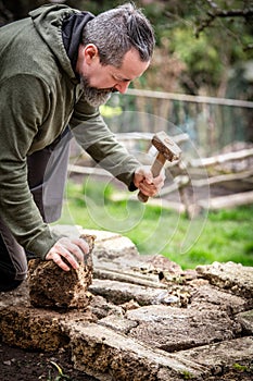 A male craftsman builds a raised bed or wall from rough stones