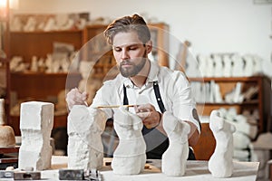 Male craftsman in working uniform makes a limestone copy of woman torso at the creative studio and show making process