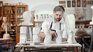 Male craftsman in working uniform makes a limestone copy of woman torso at the creative studio and show making process