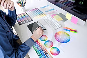 Male creative graphic designer working on color selection and color swatches, drawing on graphics tablet at workplace with work