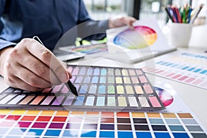 Male creative graphic designer working on color selection and color swatches, drawing on graphics tablet at workplace with work