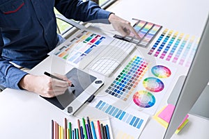 Male creative graphic designer working on color selection and color swatches, drawing on graphics tablet at workplace with work