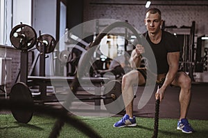 Male crossfit athlete working out with battle ropes at gym