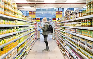 Male customer perusing food items on supermarket shelves in grocery store. Man looks at price and choose organic food