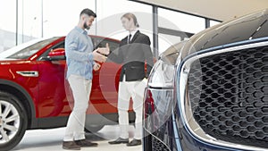 Male customer and salesman shaking hands at car dealership