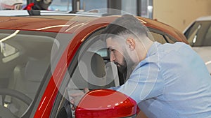 Male customer smiling to the camera while examining new car on sale
