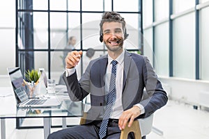 Male customer support operator with headset and smiling, with collegues at background.