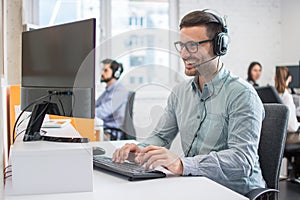 Male customer support phone operator with headset working in call centre. Group of sales agent working in office.