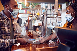 Male Customer Wearing Mask In Bar Making Contactless Payment For Drinks During Health Pandemic