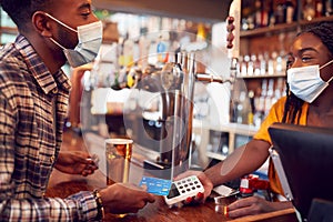 Male Customer Wearing Mask In Bar Making Contactless Payment For Drinks During Health Pandemic