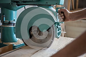 Male cutting thick wooden board with an industrial machine painted in green