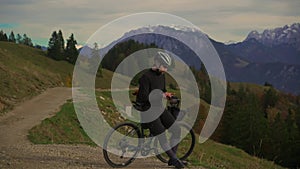 Male cyclist on gravel bicycle resting on top of mountain enjoying view cliff-top sunset in Alps in autumn and using