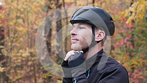 Male cyclist. Healthy young professional sportsman in activewear puts on black cycling helmet before training in fall park. Motiva