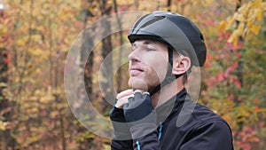 Male cyclist. Healthy young professional sportsman in activewear puts on black cycling helmet before training in fall park. Motiva