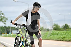 Male cyclist with injured knee carry bicycle walking in park after an accident.