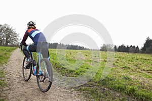 Male cyclist pauses on bike in open countryside, back view