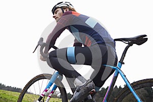 Male cyclist pauses on bike in open countryside, low angle