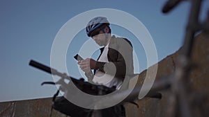 Male cyclist resting on promenade by sea and uses smartphone at sunset. Healthy active lifestyle traveler on bike