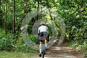 Male cyclist rides on the road of the forest on a bicycle, view from the back