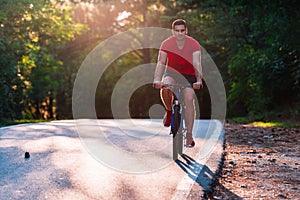 Male cyclist riding his bike on sunset on a road through deep woods. Extreme biker no safety equipment