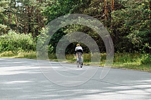 Male cyclist in sportswear rides out of town on an asphalt road in the woods