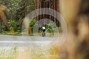 Male cyclist in sportswear trains in the woods outside the city on an asphalt road