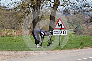 Male cyclist stretching next to a speed sign