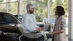 Male dealer shaking hands with african woman at auto salon