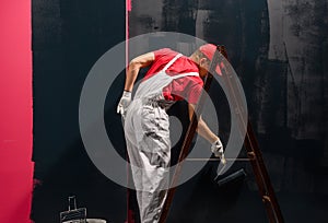 Male decorator painting a wall with black color