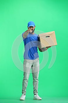 A male deliveryman, on a green background, full-length, with a box, points forward