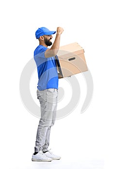 A male deliveryman, on a white background, full-length, with a box, raised his hand up