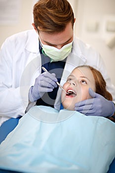 Dentist with dental mirror examining child`s teeth